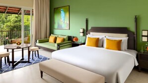 A hotel room with a bed, a sofa, a dining table, and a balcony with a view of trees. - Aurika, Coorg - Luxury by Lemon Tree Hotels (Madikeri)