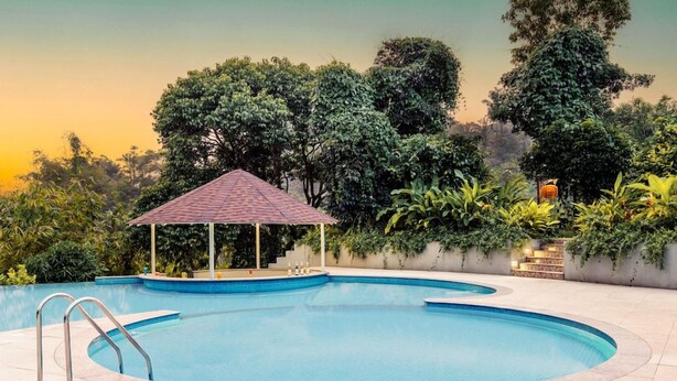 A swimming pool with a gazebo, surrounded by lush greenery and trees. - Aurika, Coorg - Luxury by Lemon Tree Hotels (Madikeri)