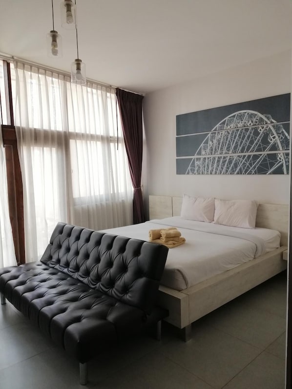 Un dormitorio con una cama, un sofá tapizado negro y una obra de arte en la pared que representa un puente.