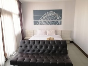 Una habitación de hotel moderna con una cama, un cabecero, una gran obra de arte de un puente y un sofá capitonado.