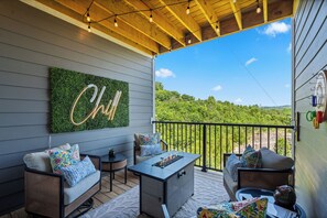 A covered outdoor seating area with a fire feature, a neon sign, and a view of a forested landscape. - Walk-In 3BR | Fun Bunk Room + Arcade | Sleeps 9 (Branson)
