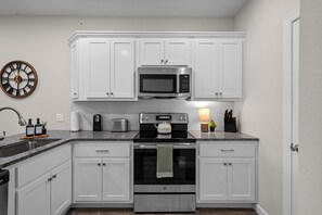 A modern kitchen with white cabinetry, a stainless steel microwave, a stove, and a toaster. - Walk-In 3BR | Fun Bunk Room + Arcade | Sleeps 9 (Branson)