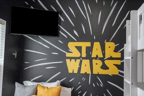A room with a Star Wars themed wall, a television, and a bed with pillows. - Walk-In 3BR | Fun Bunk Room + Arcade | Sleeps 9 (Branson)