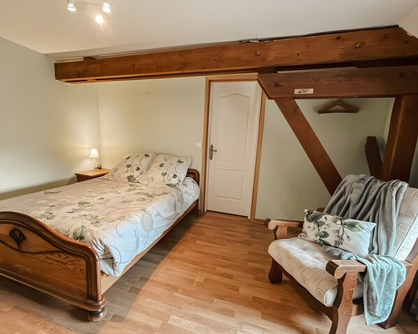 Ein Schlafzimmer mit einem hölzernen Bett, einem Sessel, einem Nachttisch und einer Tür.