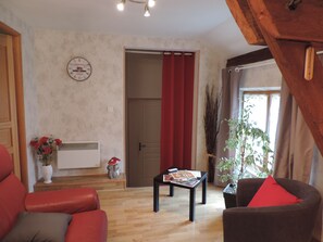 Ein Wohnzimmer mit einer Couch, einem Couchtisch mit Zeitschriften, einer Uhr an der Wand und einer Tür mit roten Vorhängen.