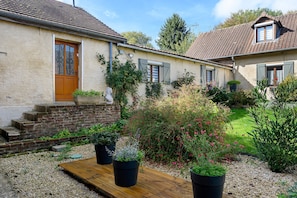 A rustic house with a wooden door, a brick staircase, and a garden with potted plants.