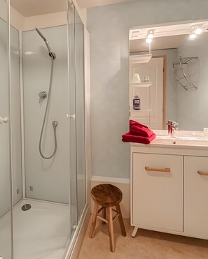 Ein Badezimmer mit einer Duschkabine, einem Waschbecken mit Spiegel und einem Hocker.