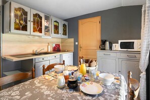 A compact kitchen with a dining table set for four, a refrigerator, a microwave, and a cabinet with glass doors.