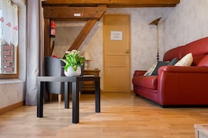 A cozy living room with a red sofa, a table with a vase of flowers, and a wooden ceiling.
