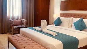 A hotel room with a large bed, a bench, a wardrobe, and a ceiling fan. - Inde Signature Jaipur (Jaipur)