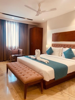 A hotel room with a large bed, a bench, a wardrobe, and a ceiling fan. - Inde Signature Jaipur (Jaipur)