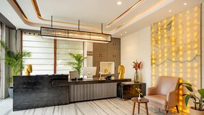 A modern reception area with a marble floor, a reception desk, a seating area with a chair, and a decorative wall with lights. - Inde Signature Jaipur (Jaipur)