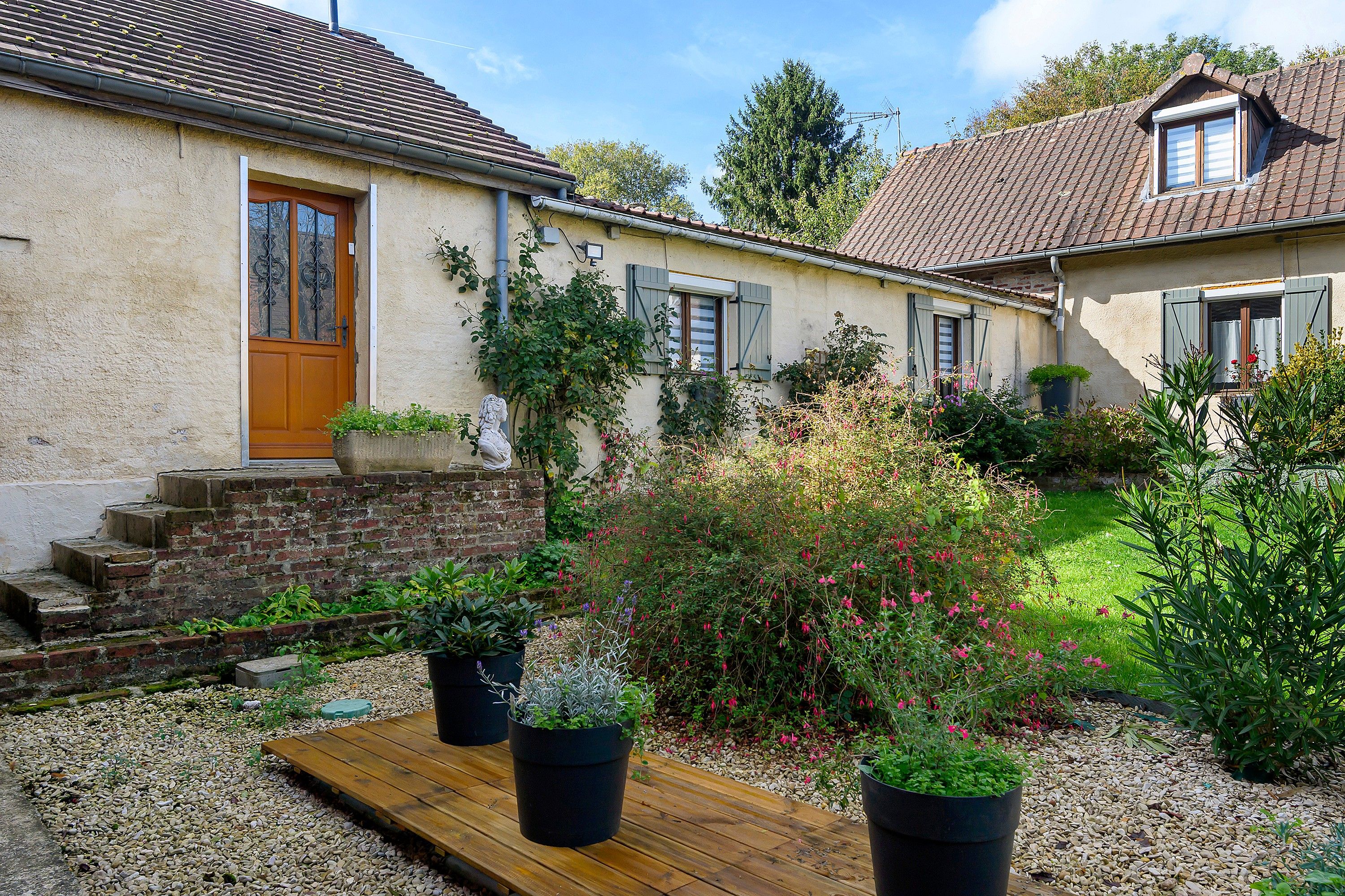 Een landelijk huis met een houten deur, een stenen trap en een tuin met potplanten.