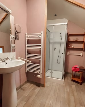 Ein Badezimmer mit Waschbecken, Spiegel, Handtuchhalter, Dusche und Holzregalen.