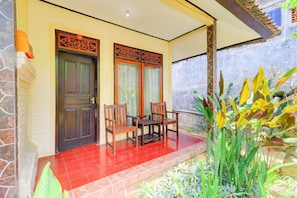 A covered outdoor seating area with a table and chairs, a door with decorative panels, and a variety of plants. - Ubud Asri by Zuzu (Ubud)