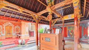 An ornate interior with traditional architectural elements, including a richly decorated ceiling and walls, and a central wooden structure with a sign. - Ubud Asri by Zuzu (Ubud)