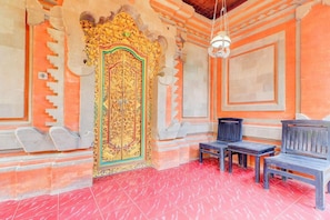 A room with a red tiled floor, a decorative door with intricate patterns, and two wooden benches.