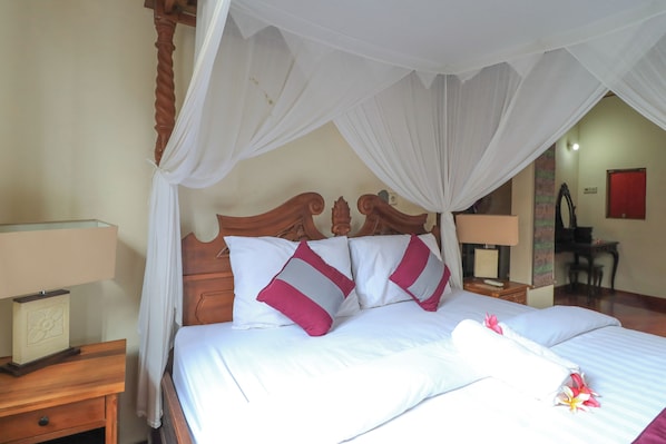 A neatly made bed with white and pink pillows, a wooden headboard, and a canopy.