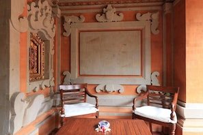 A room with two wooden chairs and a table, ornate wall decorations, and a framed picture.