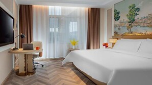 Habitación de hotel con cama, escritorio con una computadora portátil, televisión y un cuadro en la pared.