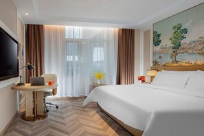 A hotel room with a bed, a desk with a laptop, a television, and a painting on the wall. - Vienna Hotel (Changping)