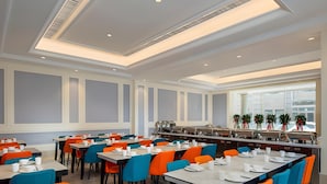 Ein moderner Essbereich mit hohen Tischen und Stühlen, einer Speiseauswahl vom Buffet und großen Fenstern.