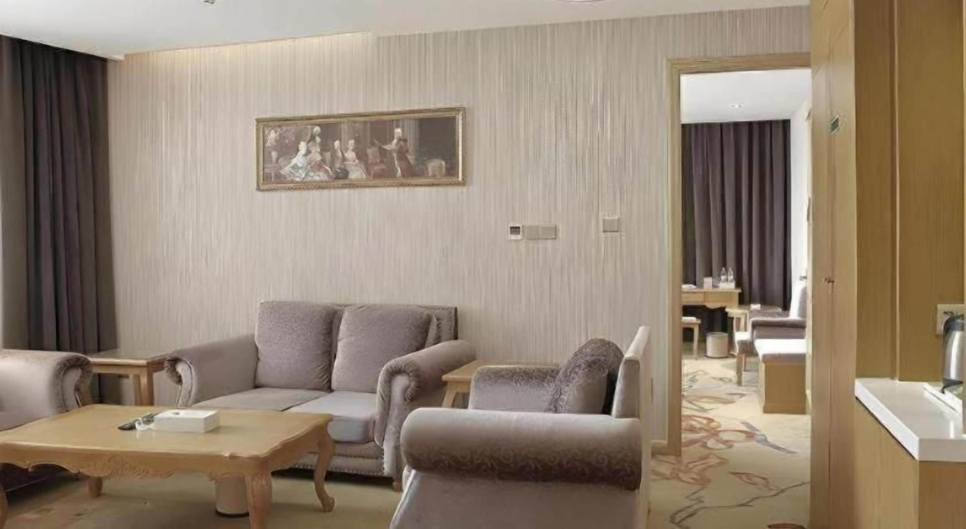 Quarto de hotel com sofá, mesa de centro, quadro na parede e vista para a sala de jantar.