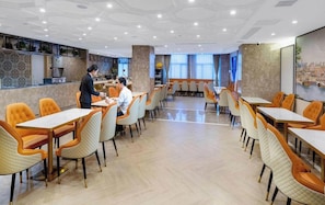 A spacious dining area with multiple tables and chairs, a bar area, and a view of the cityscape through large windows. - Vienna Hotel (Foshan)