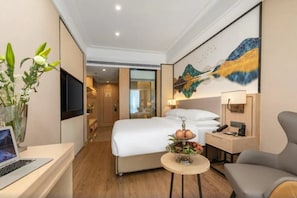 A hotel room with a bed, bedside table, lamp, chair, and a painting on the wall. - Vienna Hotel (Foshan)