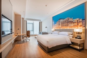 Una habitación de hotel moderna con una cama grande, un escritorio, una silla, un televisor y un mural con vista a la ciudad.