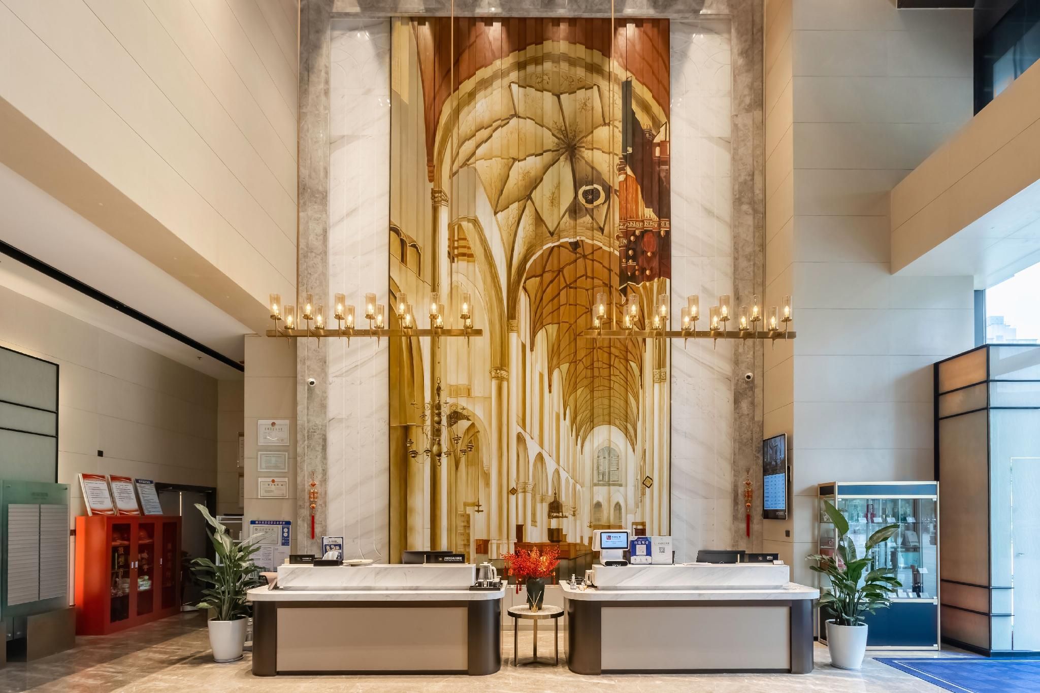 A hotel reception area with marble walls, a large mural, two reception counters, and a digital screen.