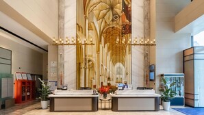 En hotellobby med väggar i marmor, en stor väggmålning, två receptionsdiskar och en digital skärm.