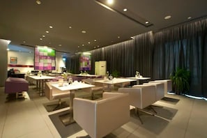 A modern hotel dining area with multiple tables and chairs, a central bar area, and a large window with curtains. - Jinjiang Inn Xinxiang Railway Station Branch (Xinxiang)