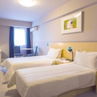 A hotel room with two beds, a desk, a chair, an air conditioning unit, and a painting on the wall.