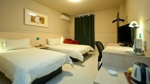 Et hotelværelse med to senge, et skrivebord, et fjernsyn og et vindue med gardiner.