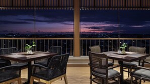 An outdoor dining area with tables and chairs, a view of the cityscape at dusk, and a wooden ceiling structure. - The Margaux Hotel Yogyakarta (Yogyakarta)
