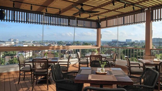 An outdoor seating area with tables and chairs, a wooden floor, and a view of the cityscape. - The Margaux Hotel Yogyakarta (Yogyakarta)