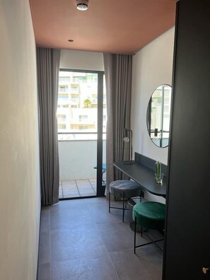 A small, modern room with a balcony, a desk, a chair, and a round mirror. - Eleven Apartments (Sliema)