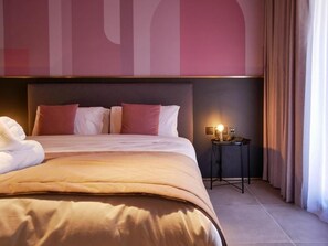 A hotel room with a large bed, a bedside table with a lamp, and a wall with a large abstract design. - Eleven Apartments (Sliema)