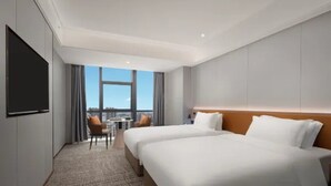 Hotellihuone, jossa on kaksi sänkyä, taulutelevisio, pieni pöytä ja tuoli sekä näkymä kaupunkiin.