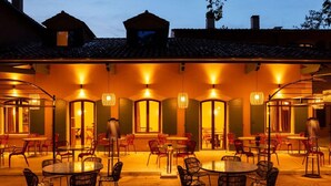 Un espacio de comedor al aire libre con mesas y sillas redondas, iluminado por lámparas colgantes.