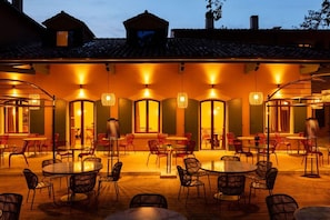 An outdoor dining area with round tables and chairs, illuminated by hanging lamps. - La Bastide Bourrelly - Mathias Dandine (Cabries)