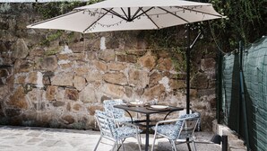 Een terras buiten, met een stenen muur, een tafel met stoelen en een parasol.