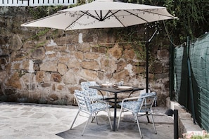 Una terrazza esterna con un muro in pietra, un tavolo e sedie, e un ombrellone.