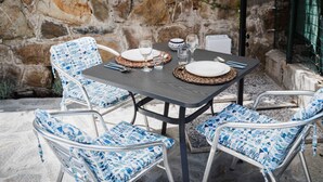 Een tafel voor vier met geweven tafelonderleggers, witte borden en blauwe gestreepte stoelen.