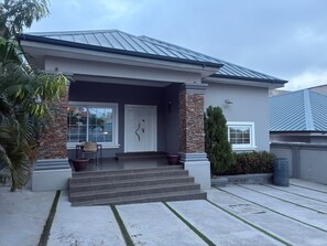 A modern two-story house with a front porch, a stone column, and a garage door. -  Heritage Comfort & Peace, Your Perfect Getaway. Self compound, gated house (Accra)