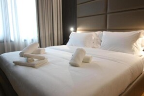 Una habitación de hotel con una cama bien hecha, cabecera y una ventana con cortinas.