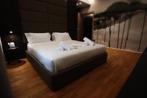 Una habitación de hotel con una cama grande, una mesita de noche con lámpara y vistas a un balcón.