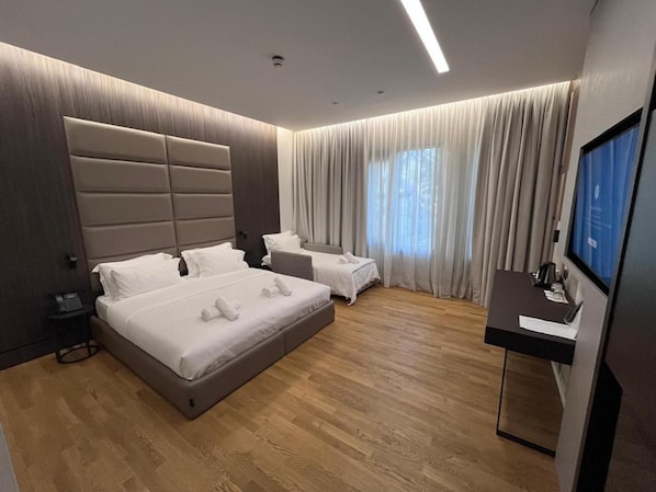 Una habitación de hotel moderna con una cama grande, una cama más pequeña, un escritorio y un televisor.