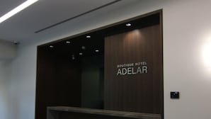 En receptionsdisk med mörk träinredning och texten ”BOUTIQUE HOTEL ADELAR” på väggen.